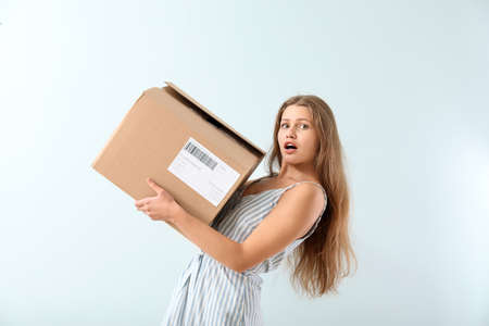 Surprised woman with cardboard box on light backgroundの写真素材