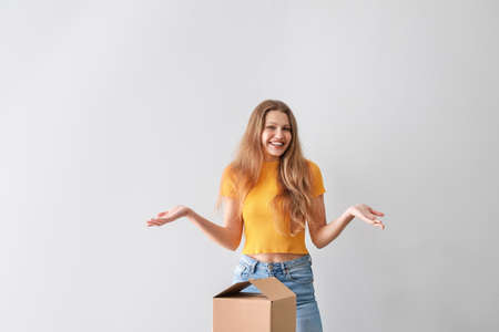 Young woman with cardboard box on light background