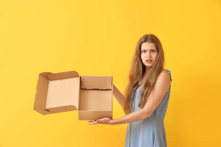 Displeased woman with empty cardboard box on color background