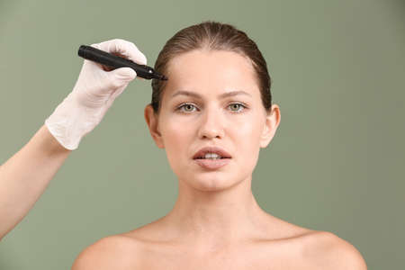Plastic surgeon applying marking on female face against color background