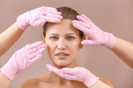 Plastic surgeons touching face of young woman on color backgroundの写真素材