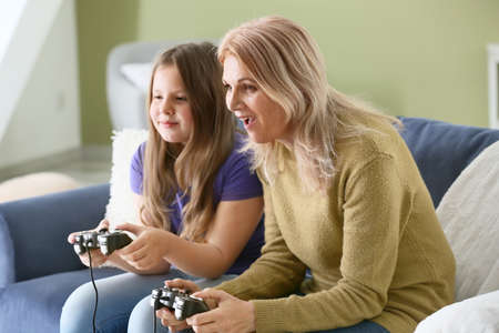 Mature woman and her cute granddaughter playing video game at home