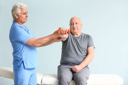 Mature physiotherapist working with senior man on light backgroundの写真素材