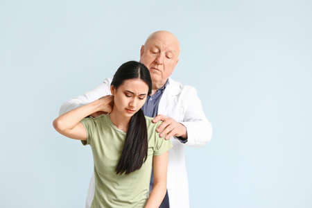 Senior physiotherapist working with young Asian woman on light background