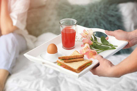 Young woman receiving breakfast in bed from her beloved husband