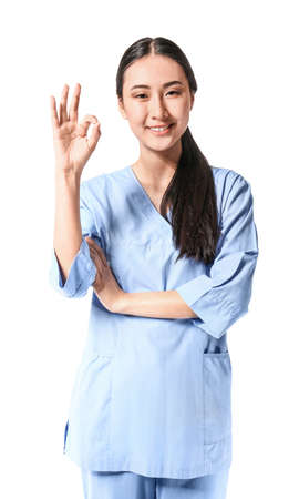 Portrait of young Asian physiotherapist showing OK gesture on white backgroundの写真素材