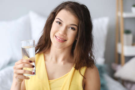 Beautiful young woman with glass of water at home