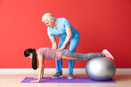Mature physiotherapist working with young Asian woman in clinic