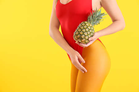 Beautiful young woman in swimming suit and with pineapple on color backgroundの写真素材