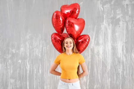 Beautiful young woman with heart-shaped air balloons against grunge wall