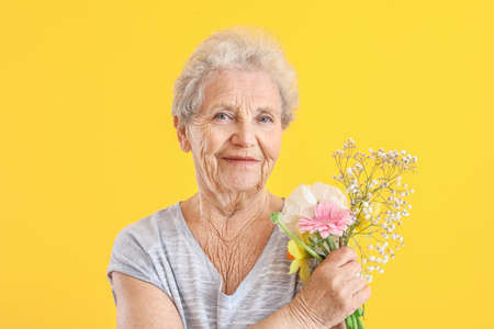 Portrait of senior woman with bouquet of flowers on color backgroundの写真素材