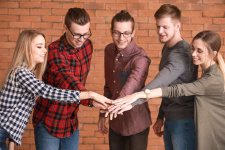 Group of young business people putting hands together on brick background