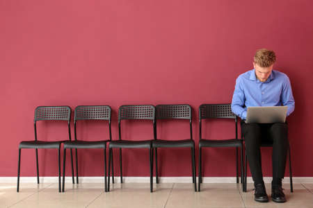 Young man with laptop waiting for job interview indoorsの写真素材