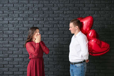 Young man greeting with air balloons his wife near dark brick wallの写真素材