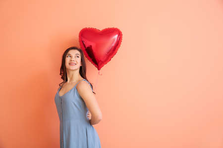 Beautiful young woman with heart shaped air balloon on color backgroundの写真素材