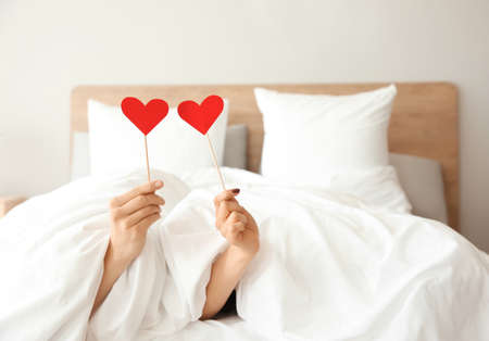 Happy young couple with paper hearts lying in bedの写真素材