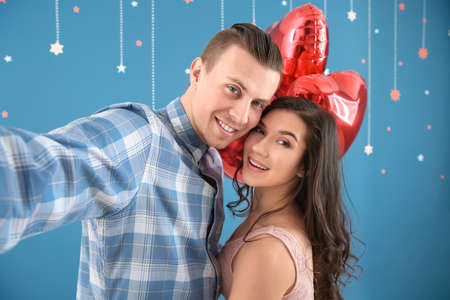 Happy young couple with air balloons taking selfie on color background