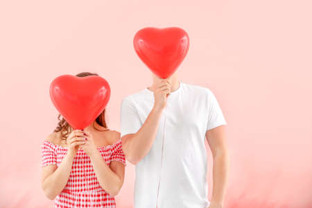 Happy young couple with air balloons on color background