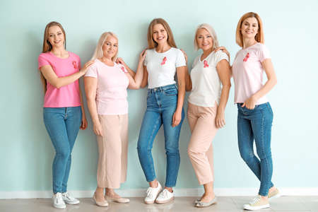 Beautiful women of different ages with pink ribbons near light wall. Breast cancer concept