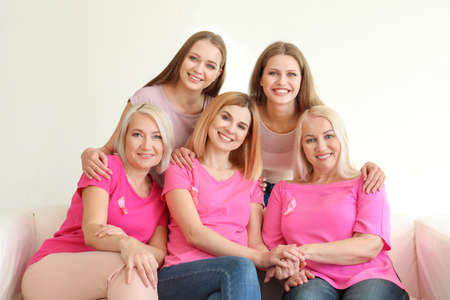 Beautiful women of different ages with pink ribbons sitting on sofa in room. Breast cancer conceptの写真素材