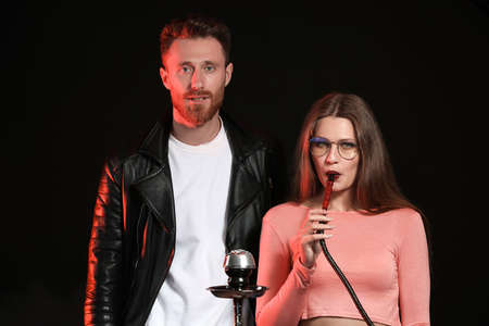Young couple smoking hookah on dark background