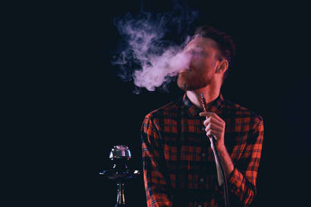 Young man smoking hookah on dark backgroundの写真素材