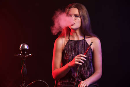 Young woman smoking hookah on dark backgroundの写真素材