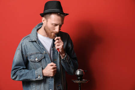 Young man smoking hookah on color background
