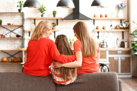 Happy girl with her mother and grandmother sitting on sofa at home, back viewの写真素材