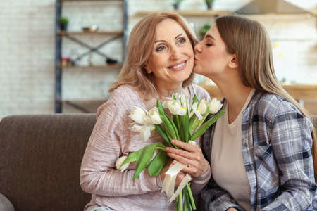 Happy daughter greeting her mother with bouquet of flowers at homeの写真素材