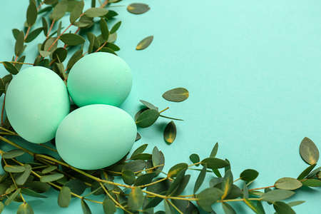 Beautiful Easter eggs with green leaves on color background