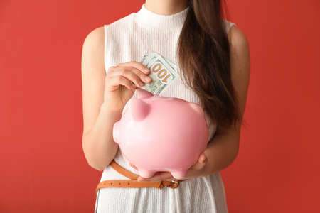 Young woman with piggy bank and money on color background