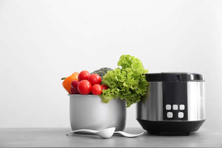 Modern multi cooker with vegetables on table against light background