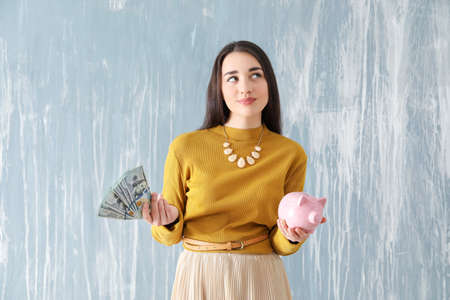Thoughtful woman with piggy bank and money on grunge backgroundの写真素材