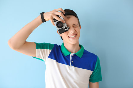 Teenage boy with photo camera on color background