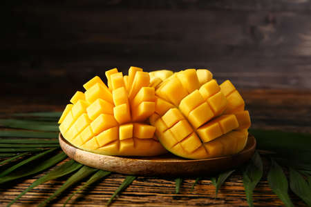 Plate with tasty fresh mango and tropical leaves on wooden tableの写真素材