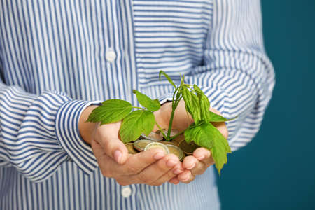 Woman holding coins and young plant on color background, closeup. Money savings concept