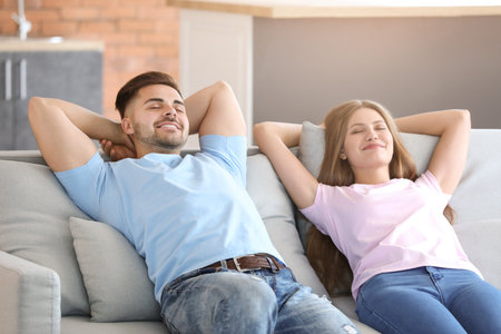Happy young couple resting together on sofa at homeの写真素材
