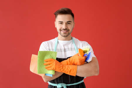 Happy young man with cleaning supplies on color backgroundの写真素材
