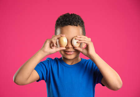 Little African-American boy with Easter eggs on color background
