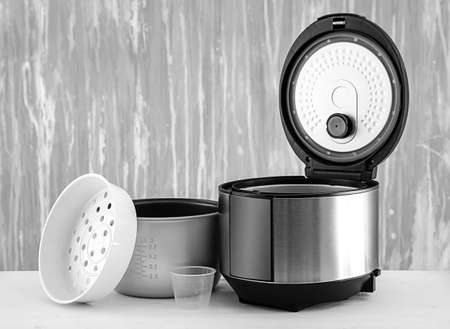 Modern multi cooker with accessories on table against gray background