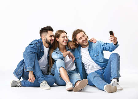Stylish young people in jeans clothes taking selfie on white background