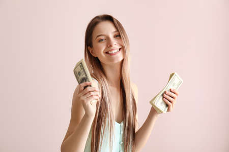 Happy young woman with money on color backgroundの写真素材