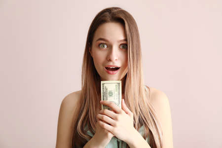 Surprised young woman with money on color backgroundの写真素材