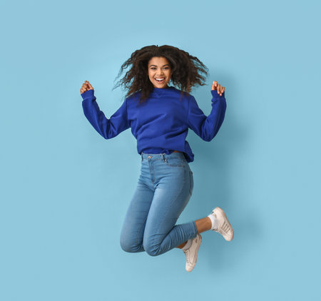 Jumping African-American woman on color background