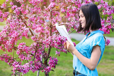 Beautiful young woman reading book in park