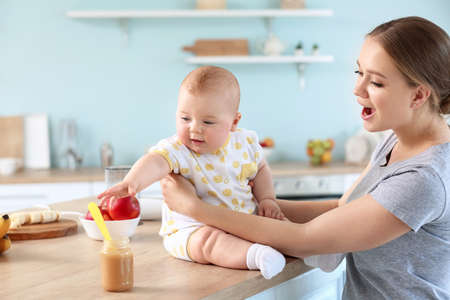 Mother feeding her little baby in kitchen at homeの写真素材