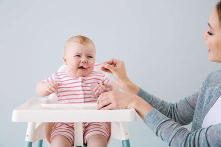 Mother feeding her little baby on gray background