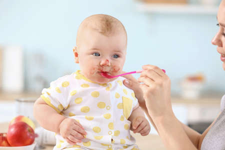 Mother feeding her little baby in kitchen at homeの写真素材