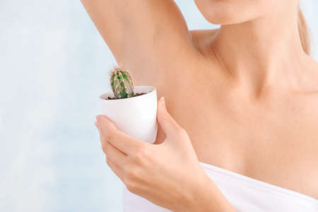 Beautiful young woman with cactus on light background. Depilation concept